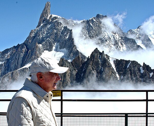 Papst Benedikt im Urlaub in den Bergen. Er trägt eine Schildkappe, die Berge im Hintergrund sind ganz leicht mit Schnee bedeckt. Es ist strahlend blauer Himmel.