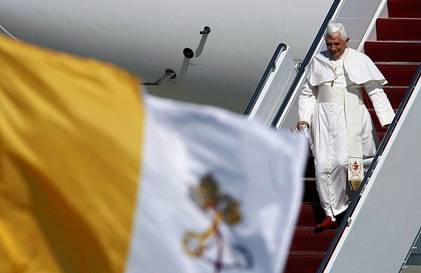 Papst Benedikt XVI. steigt aus dem Flugzeug. Im Vordergrund ist eine gelb weiße Flagge zu sehen.