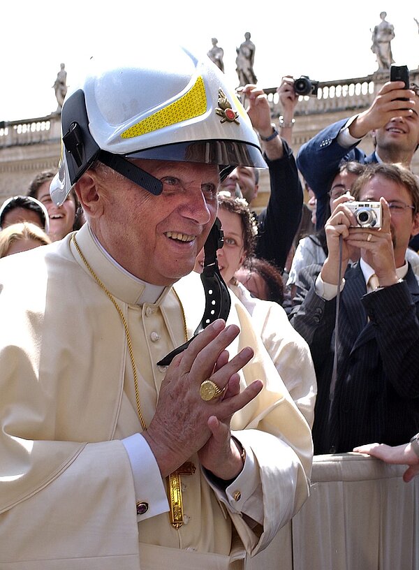 Papst Benedikt XVI. trägt einen Feuerwehrhelm.